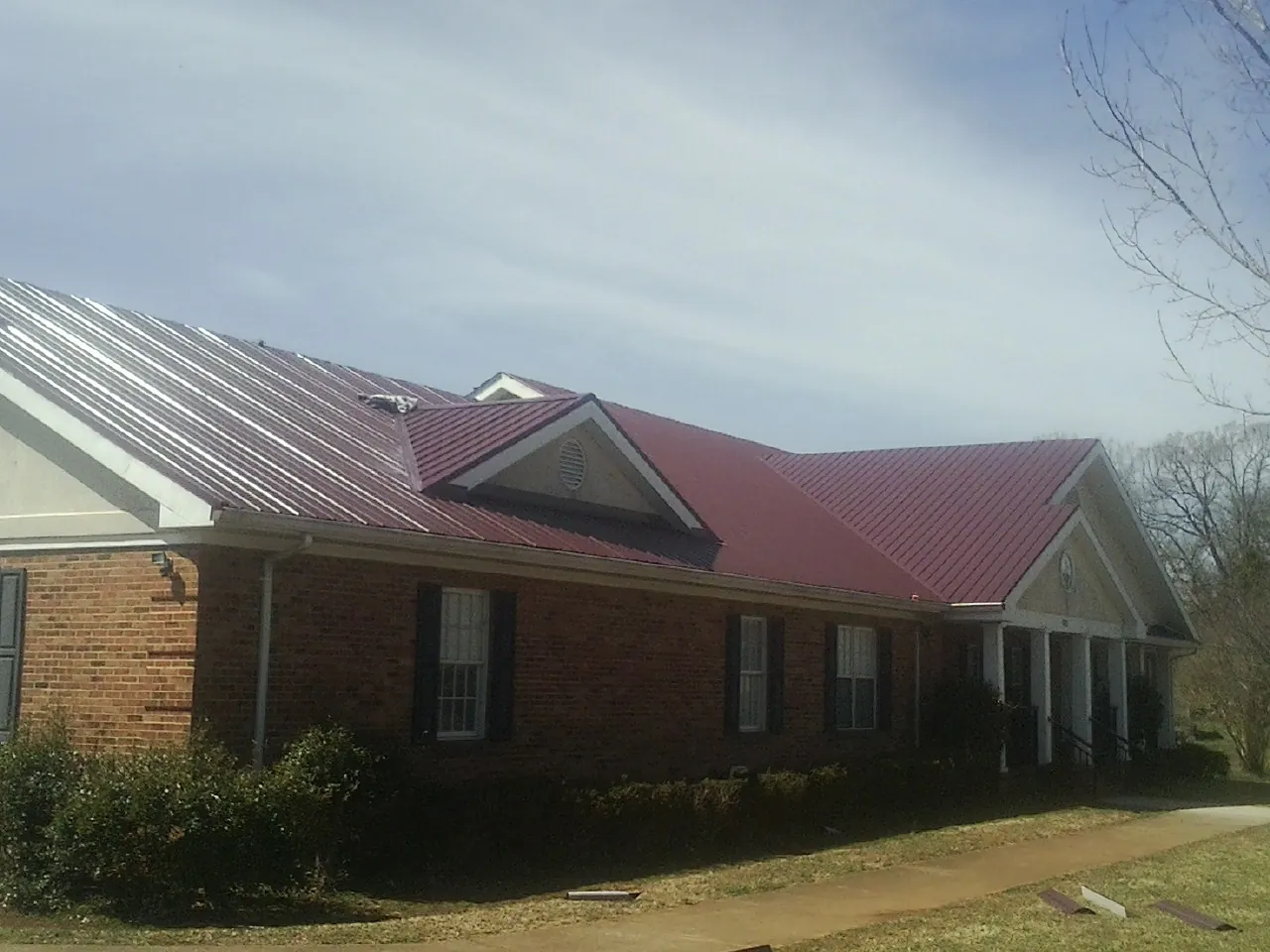 Red metal roof with gabled entries on a long brick building, from a Hail Damage Roof Repair job in Liberty Center