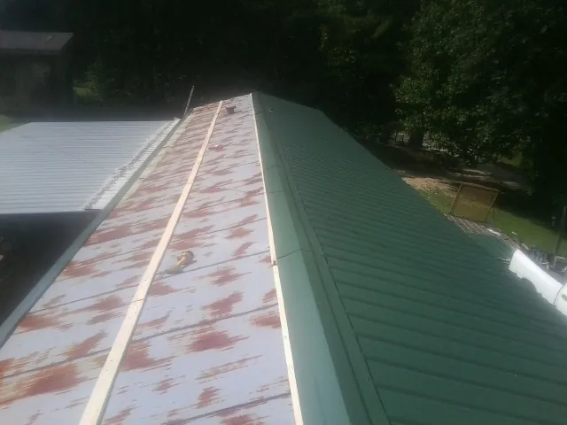 Old rusted panels beside newly installed green metal roofing — Wind Damage Roof Repair by Roofing Brothers in Liberty Center