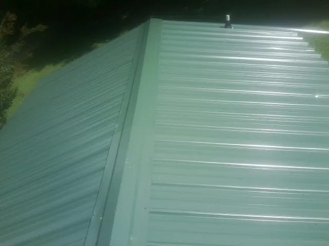 New green metal panels meeting at the ridge of a roof — Flat Roof Repair work by our crew in Liberty Center