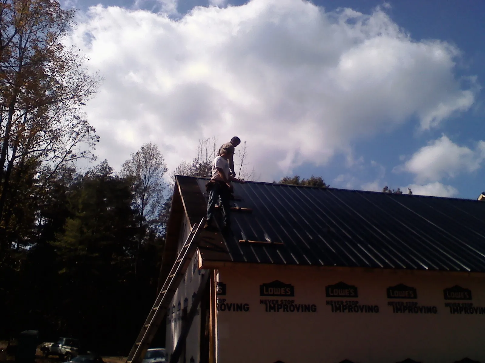 Roofer fastening dark metal panels high against a cloudy sky, from a Roof Inspection job in Liberty Center